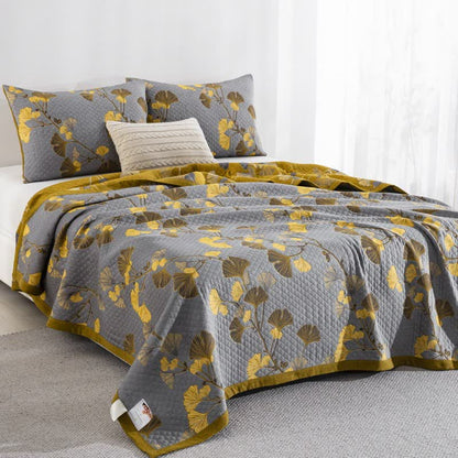 Gray ginkgo quilt on a bed at an angle with yellow and brown leaves, matching pillowcases and the mustard reverse and border