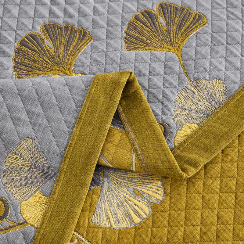 Close-up of a folded corner, gray diamond quilting with yellow ginkgo leaves over the mustard reverse and border band