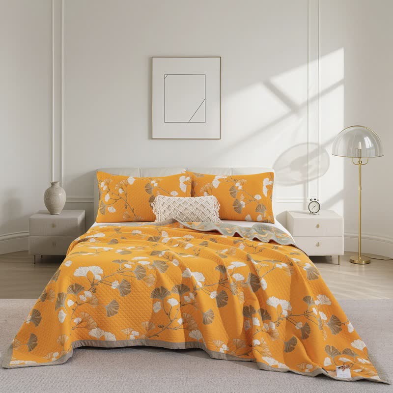 Orange ginkgo quilt spread over a bed with white and taupe leaves, matching pillowcases and a sage gray border