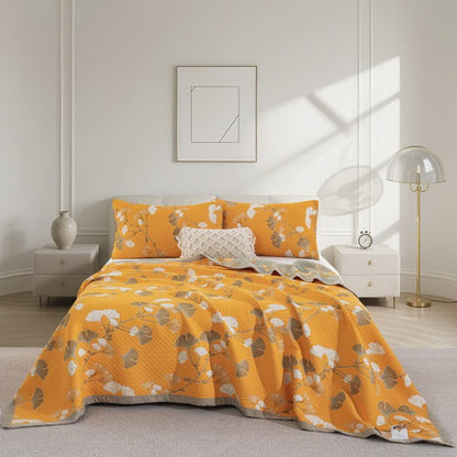 Orange ginkgo quilt spread over a bed with white and taupe leaves, matching pillowcases and a sage gray border