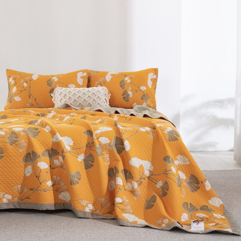Orange ginkgo quilt draped over a bed, the sage gray reverse turned back at the head, with matching pillowcases