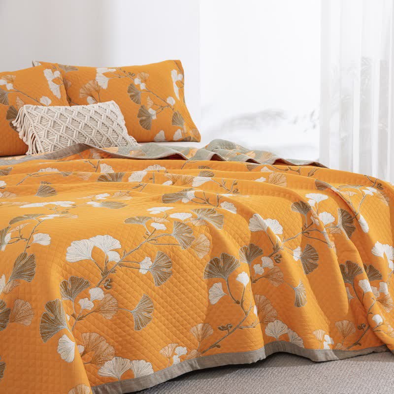 Orange ginkgo branch quilt with white and brown leaves on a bed, matching pillowcases and a sage reverse at the side