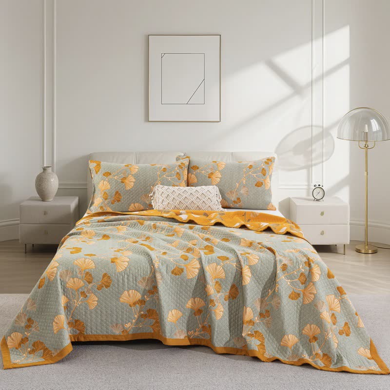 Pale sage gray ginkgo quilt with orange and cream leaves on a bed, matching pillowcases and an orange border