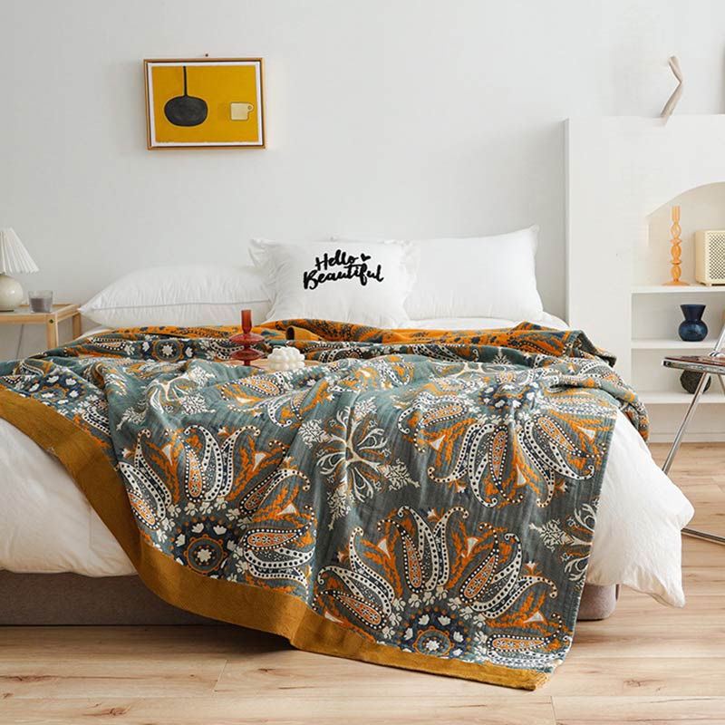 Dark teal floral cotton quilt spread over a bed, orange and white paisley medallions with a wide mustard border and the orange reverse at the head