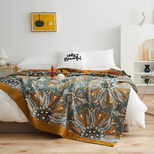 Dark teal floral cotton quilt spread over a bed, orange and white paisley medallions with a wide mustard border and the orange reverse at the head