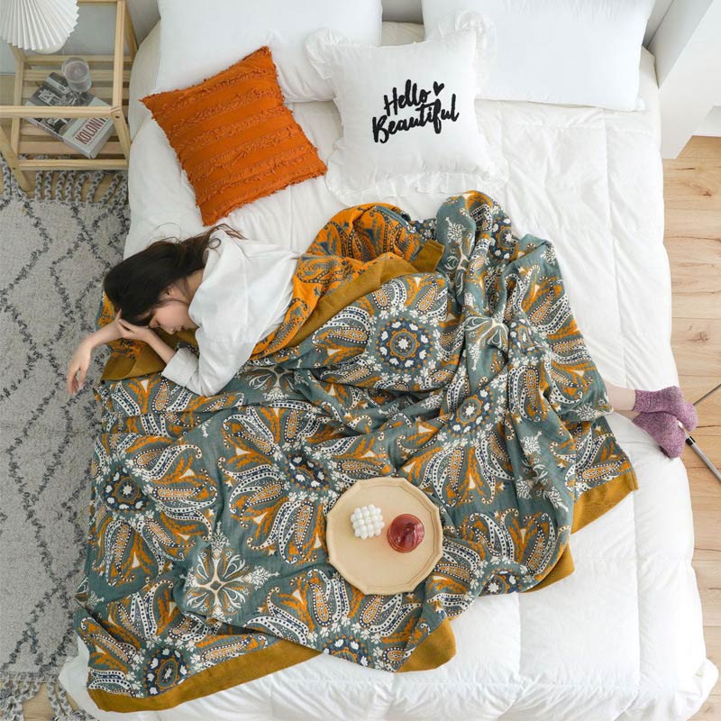 Paisley medallion quilt draped over a woman asleep across a bed, seen from above, the orange reverse along the top edge
