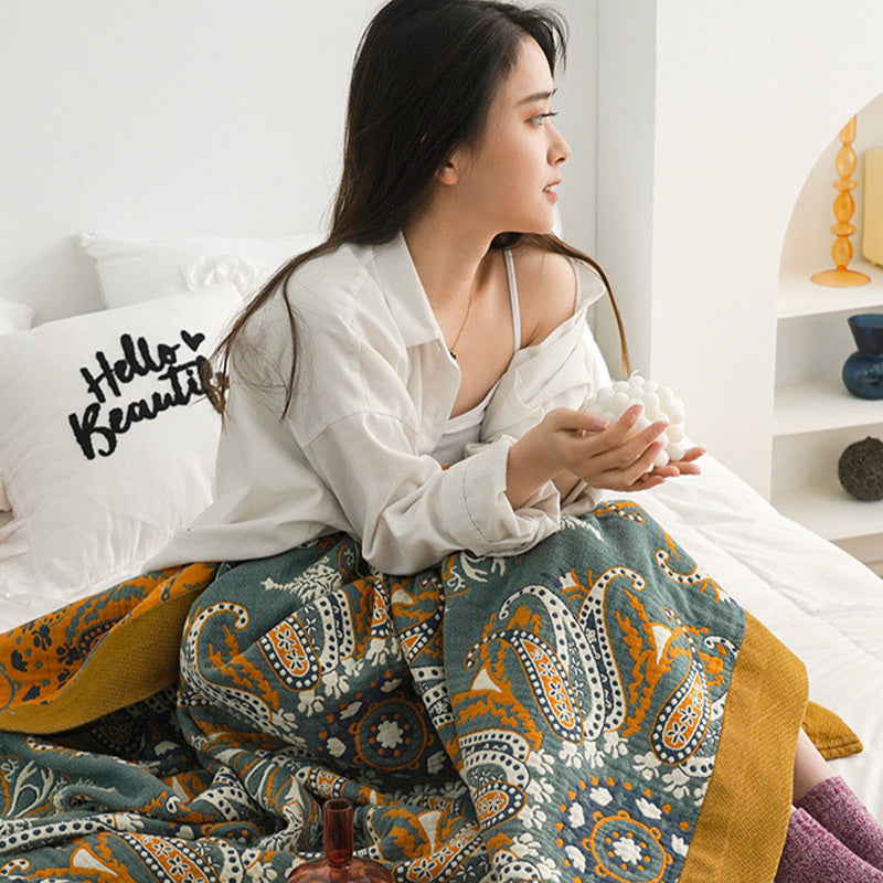 Woman sitting up in bed with the teal paisley quilt over her legs, the orange reverse and mustard border at one side
