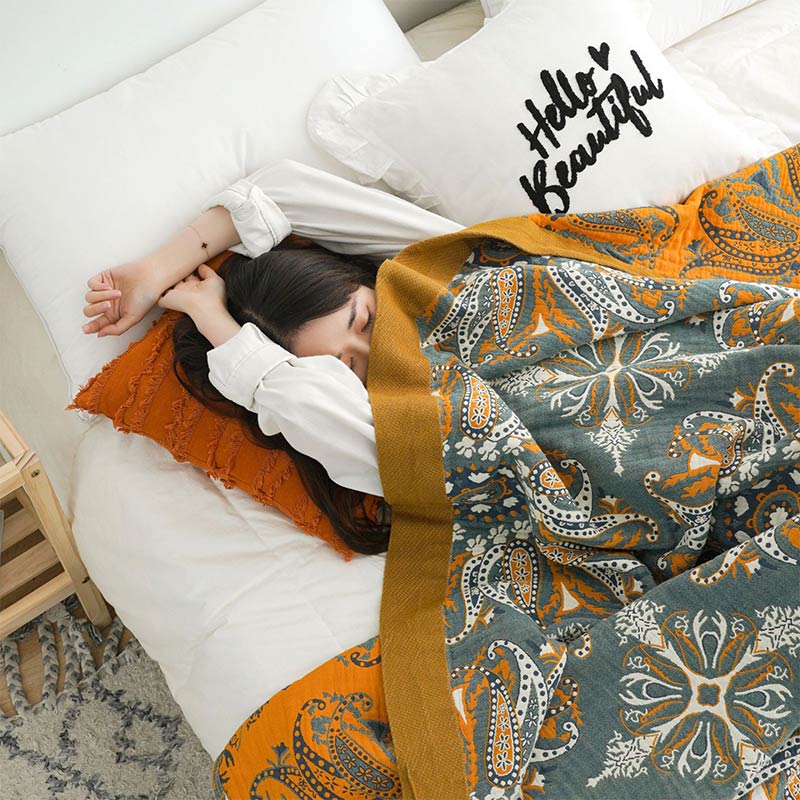 Teal and orange paisley quilt pulled up to the shoulder of a sleeping woman, the mustard border running along its edge