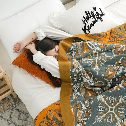 Teal and orange paisley quilt pulled up to the shoulder of a sleeping woman, the mustard border running along its edge