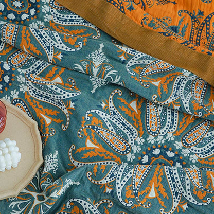 Dark teal paisley cotton quilt crumpled on a bed, the mustard border and the bright orange reverse turned back at one corner