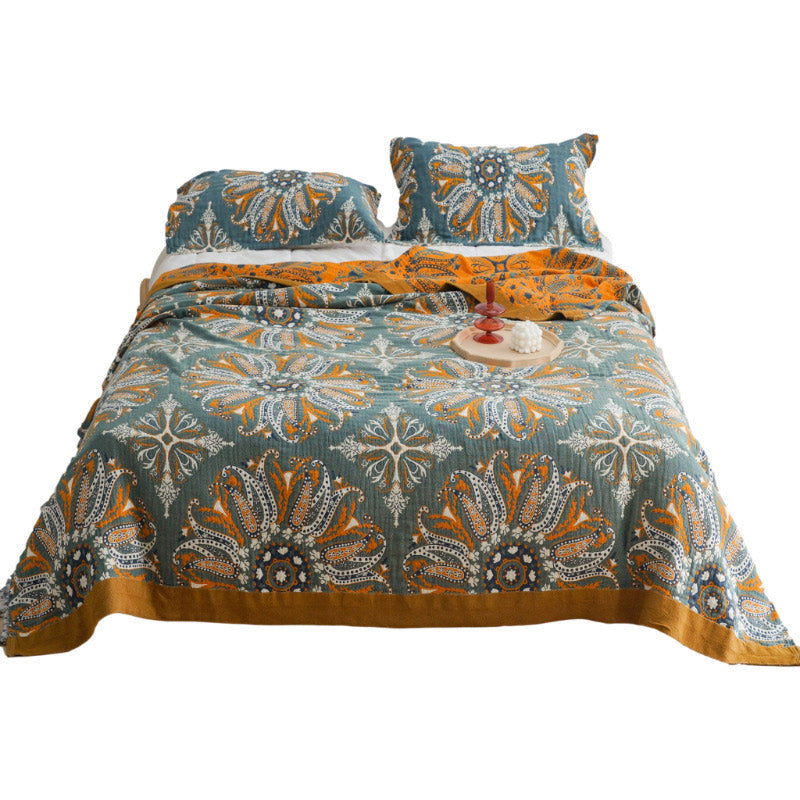 Dark teal paisley quilt laid over a bed on a white background, the mustard border framing the design
