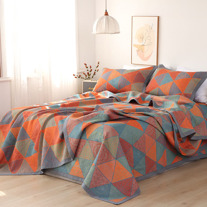 Orange and blue triangle quilt draped over a bed in a bright bedroom with two pillowcases