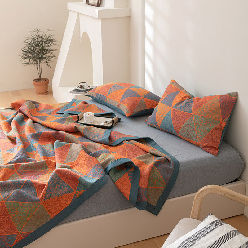 Soft three layer cotton quilt loosely draped on a bed in orange, blue and sage triangles
