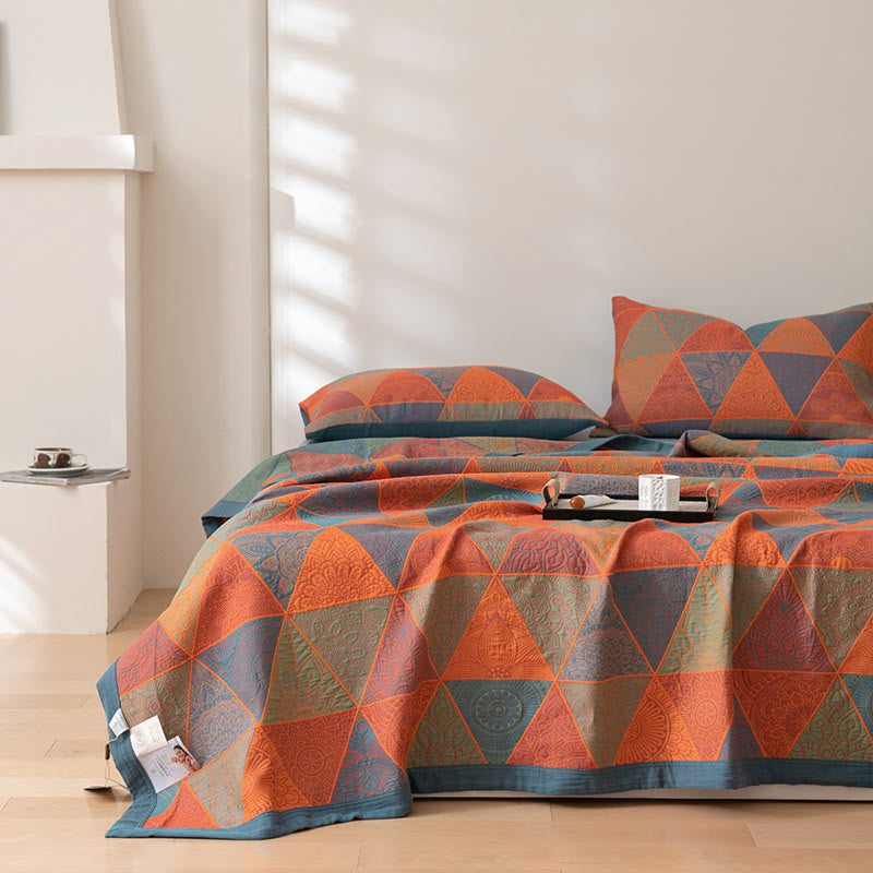 Orange and blue triangle quilt spread down to the foot of a bed with two matching pillowcases in afternoon sunlight