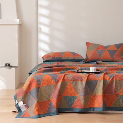 Orange and blue triangle quilt spread down to the foot of a bed with two matching pillowcases in afternoon sunlight