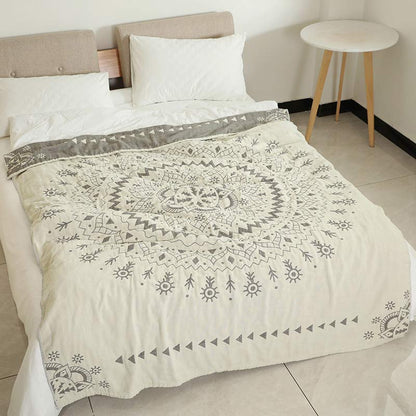 Cream cotton quilt with a large gray mandala spread over a bed, its dark gray reverse turned back at the head