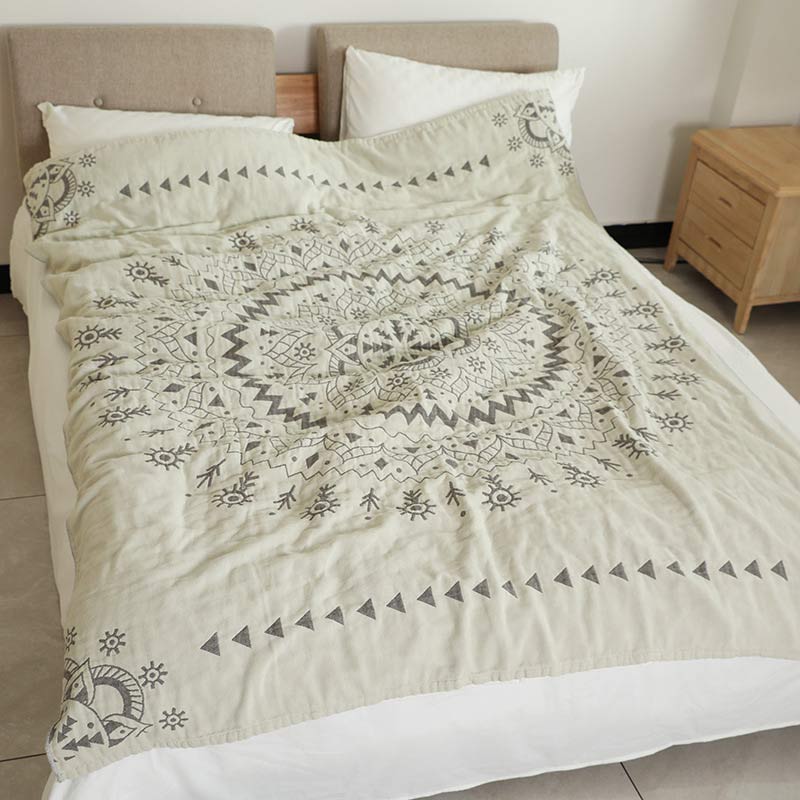 Gray mandala cotton quilt laid over a bed, the zigzag and petal rings centered and a row of triangles near the foot