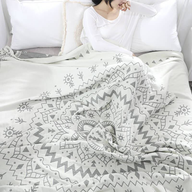 Woman sitting up in bed under the gray mandala quilt, the dark gray reverse showing along the top edge