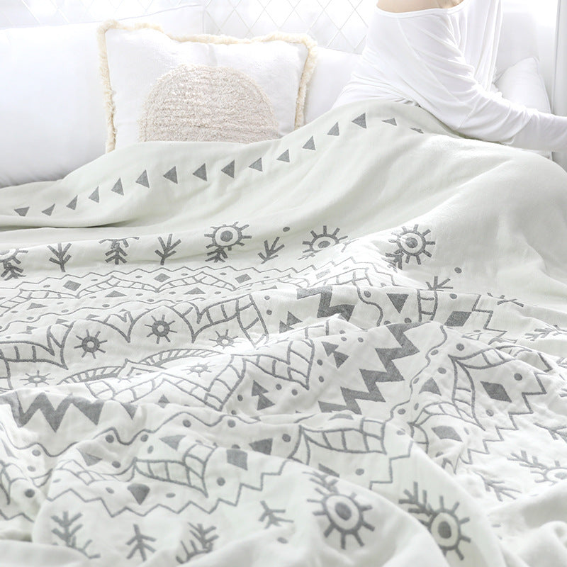 Gray mandala quilt rumpled over a bed, a row of triangles and sun motifs across the top