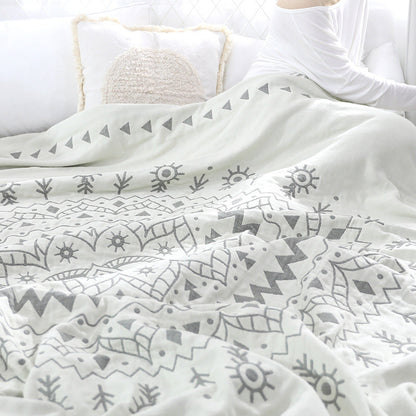 Gray mandala quilt rumpled over a bed, a row of triangles and sun motifs across the top
