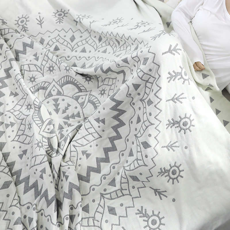 Gray mandala quilt falling in loose folds across a bed, the petal rings and sun motifs large in the frame