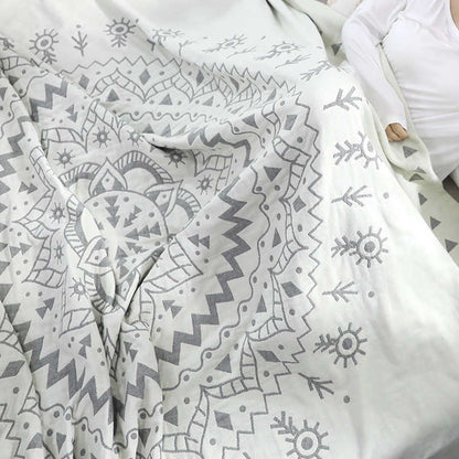 Gray mandala quilt falling in loose folds across a bed, the petal rings and sun motifs large in the frame