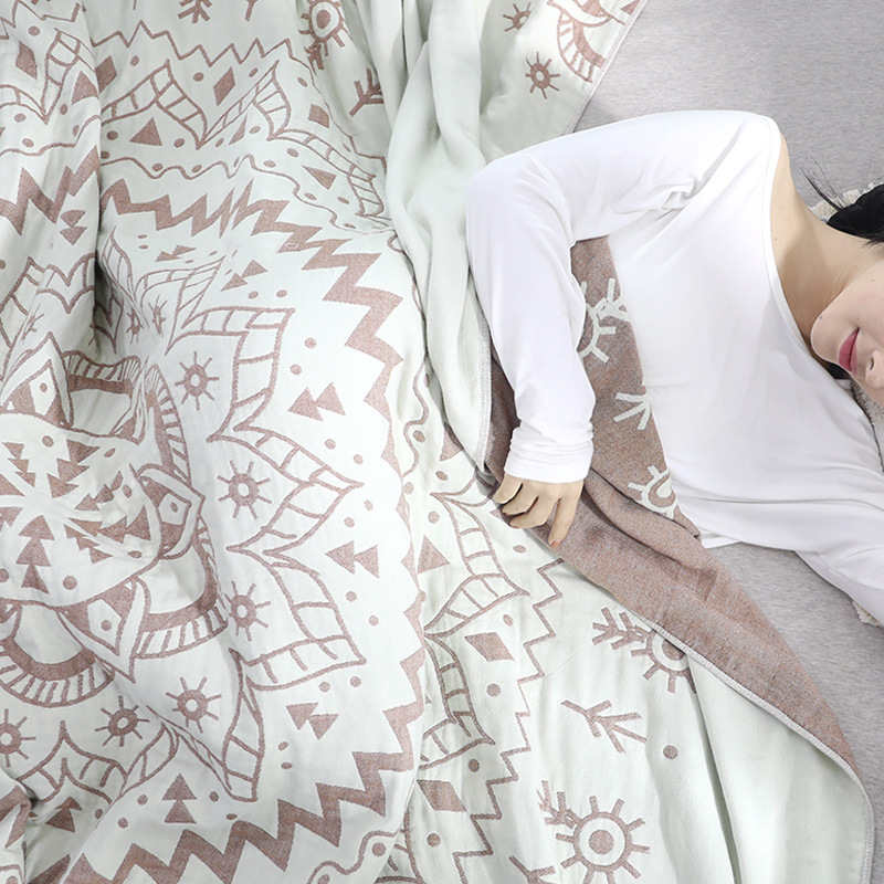 Woman lying under the brown mandala quilt, the rose-brown reverse folded back beside her arm