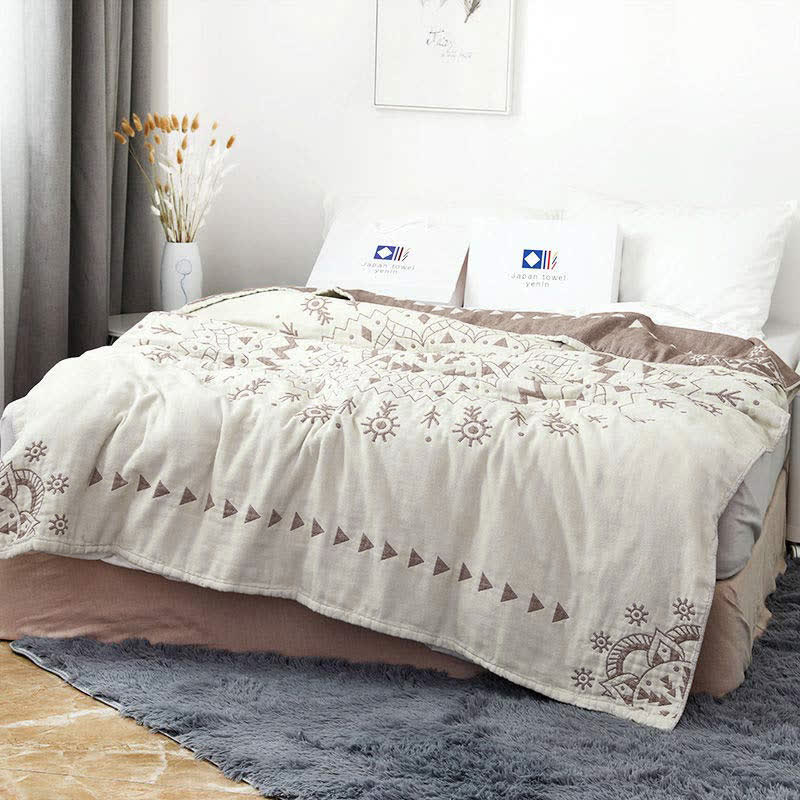 Brown mandala cotton quilt over a bed, rose-brown triangles and corner motifs on cream with the reverse turned back at the head