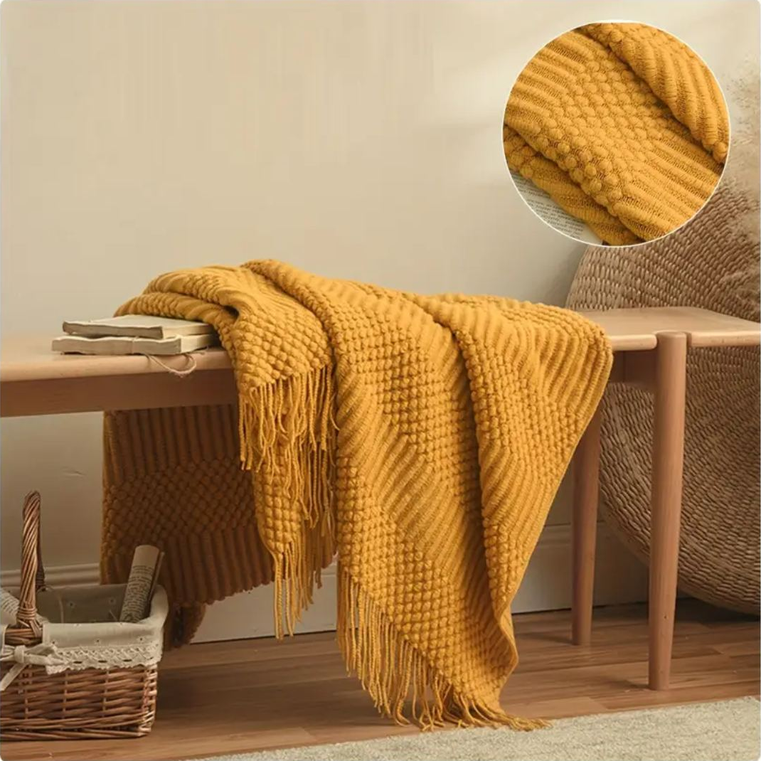 Mustard textured knit throw draped long over a bench, tassels hanging from both folds, with a round close-up of the popcorn knots and ribs