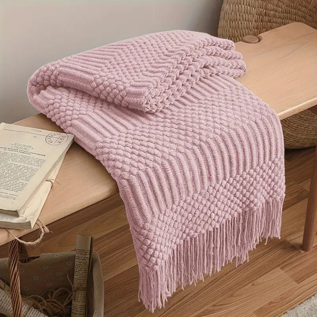 Dusty pink knit throw blanket with popcorn and rib bands folded over a wooden bench