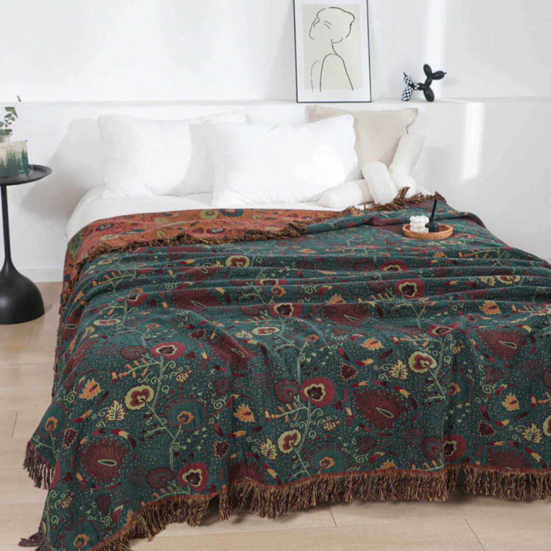 Dark green floral cotton blanket spread over a bed, burgundy and cream flowers on pale vines, the rust reverse folded back at the pillows
