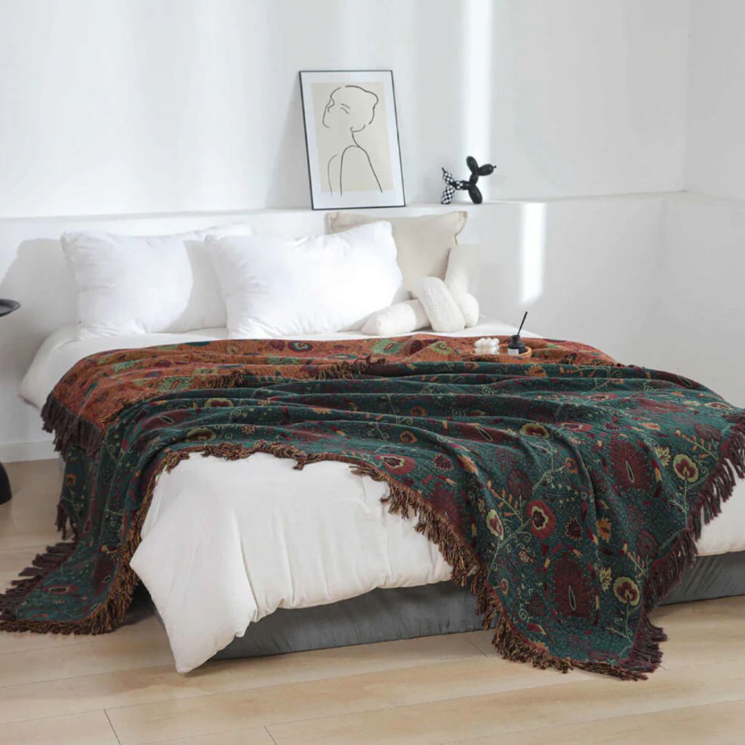 Green floral blanket thrown across a white duvet, the rust-orange reverse showing at the head of the bed and fringe hanging over both sides