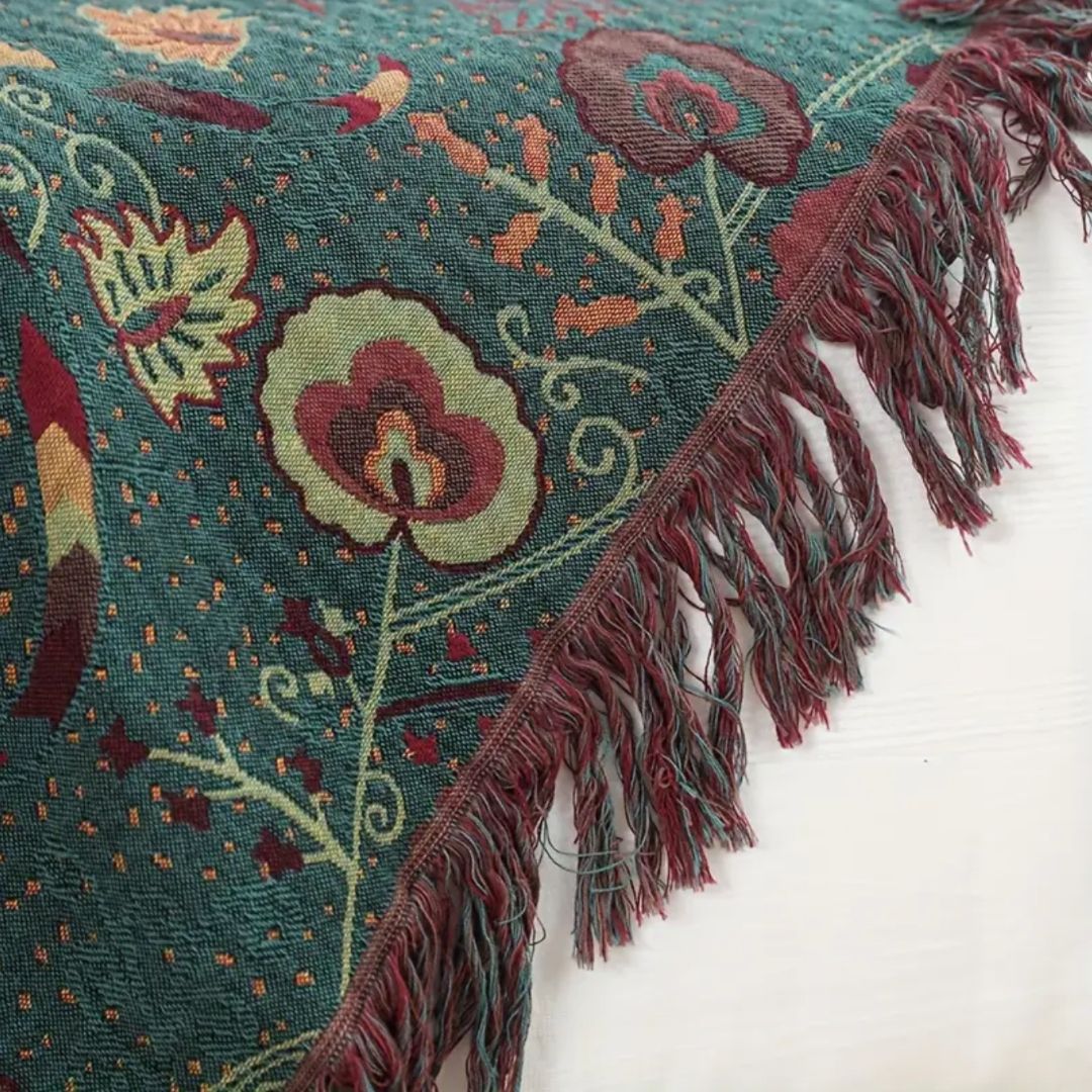 Close-up of the woven teal-green face, a round cream and burgundy flower on pale curling vines, gold dots and a burgundy fringe