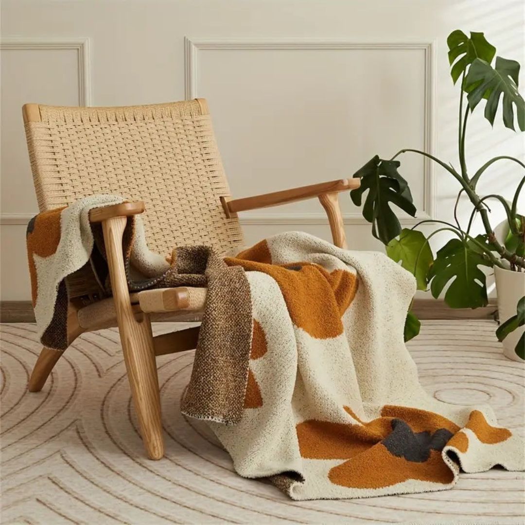 Retro flower knit throw draped over a rattan armchair, rust flowers on speckled cream with the brown back showing in the folds