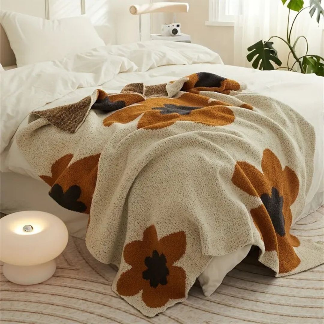 Plush knit throw with large rust and charcoal flowers draped over the foot of a bed with white bedding