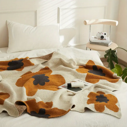 Retro flower knit blanket spread across a bed, big rust flowers with charcoal centers on a speckled cream ground