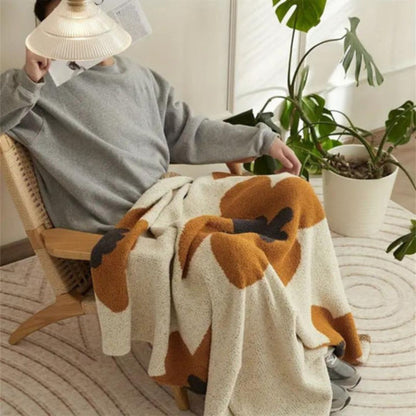 Soft rust and cream flower throw over the lap of someone reading in a rattan armchair