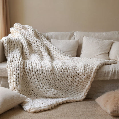 White chunky knit throw draped over a linen sofa and spilling onto the floor, its big rounded loops catching the light