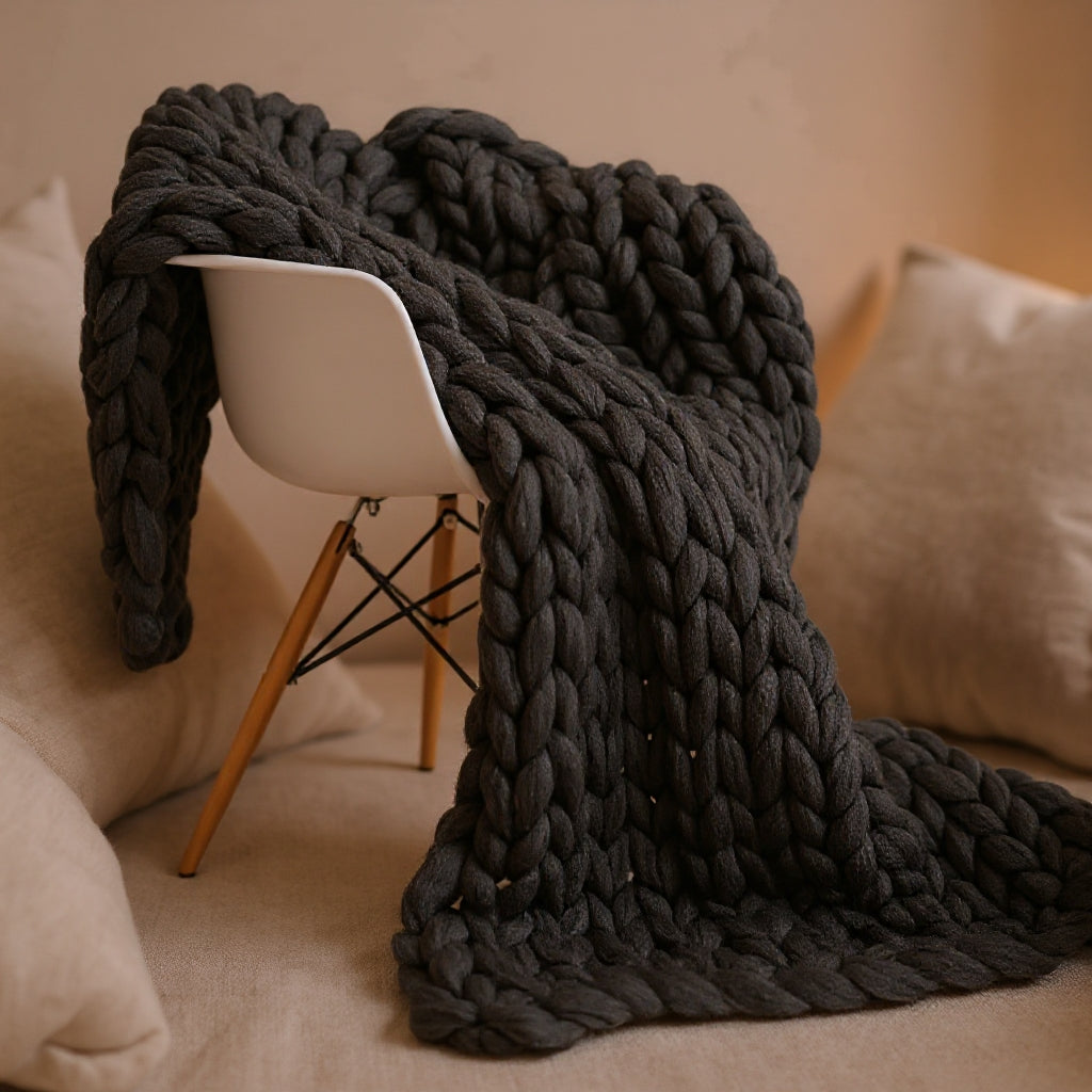 Charcoal chunky knit throw hanging over a white shell chair, the heathered loops falling in deep folds to the seat