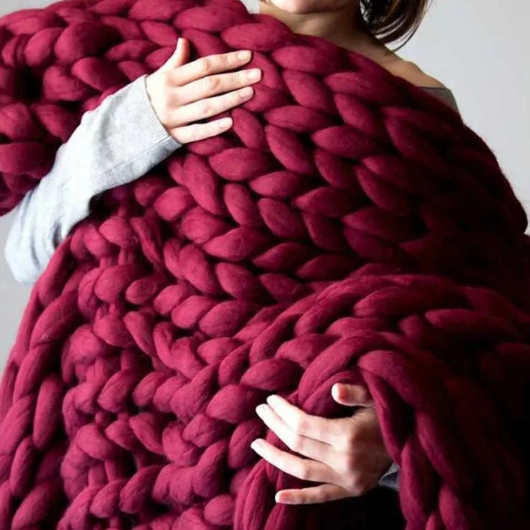 Burgundy chunky knit throw held in a person's arms, the deep wine-red loops filling the frame