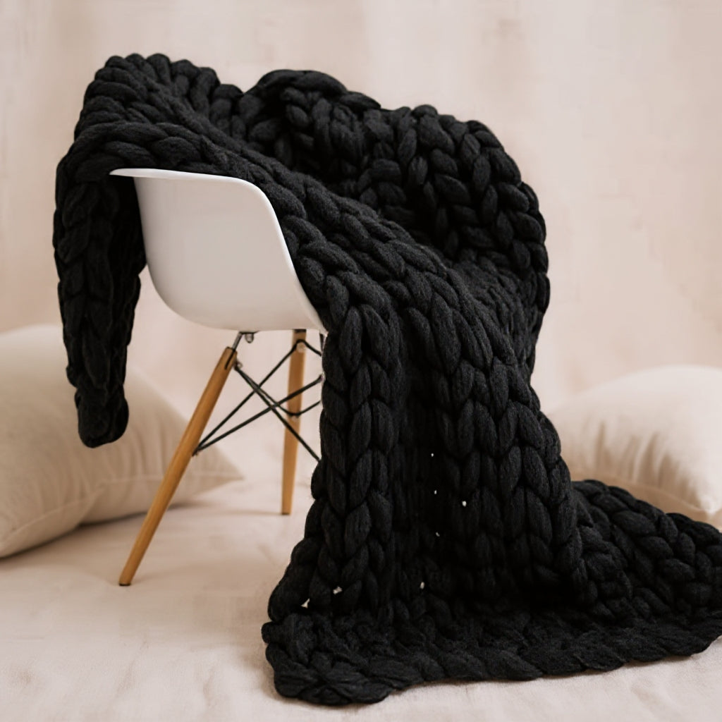 Black chunky knit throw draped over a white shell chair against a pale wall