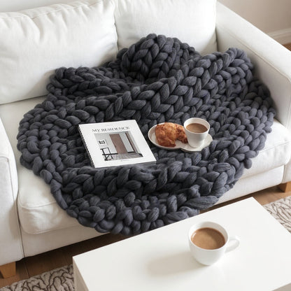 Charcoal chunky knit throw spread across a white sofa, with a magazine, a croissant and a cup of coffee resting on the loops