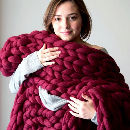 Smiling woman hugging a burgundy chunky knit throw to her chest, the deep wine-red loops wrapped around her arms