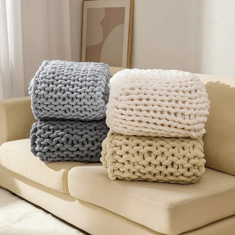 Four chunky chenille knit throws folded in two stacks on a sofa, in silver, gray, white and beige