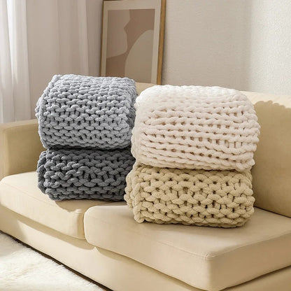 Four chunky chenille knit throws folded in two stacks on a sofa, in silver, gray, white and beige