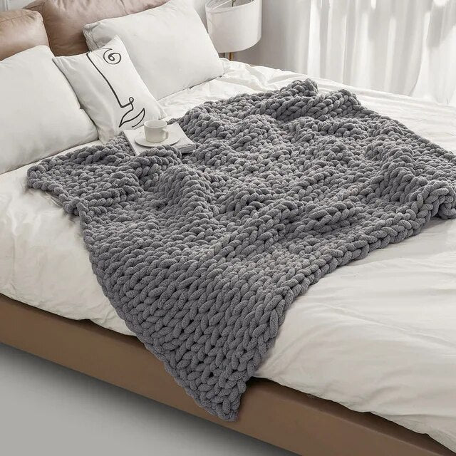 Gray chunky chenille knit throw spread across a white bed, the loose loops falling over the side