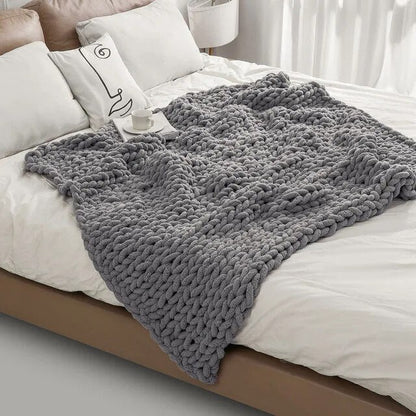 Gray chunky chenille knit throw spread across a white bed, the loose loops falling over the side