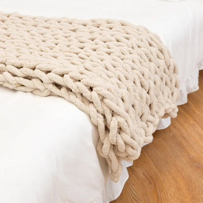 Beige chunky chenille throw hanging over the end of a white bed, the soft pile visible on every loop