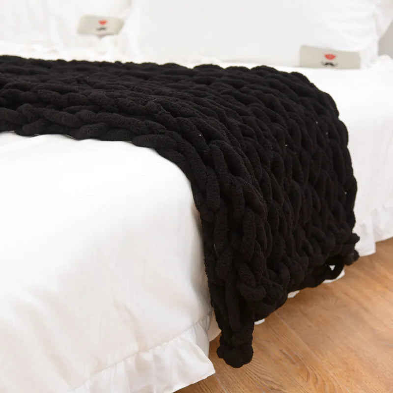 Black chunky chenille knit throw hanging over the end of a white bed, its loops falling to the floor
