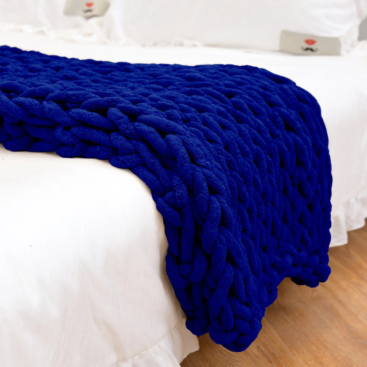 Royal blue chunky chenille knit throw hanging over the end of a white bed